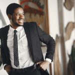 Homme souriant en costume ajustant sa ceinture, exsudant la confiance dans un cadre intérieur.