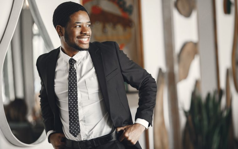 Homme souriant en costume ajustant sa ceinture, exsudant la confiance dans un cadre intérieur.