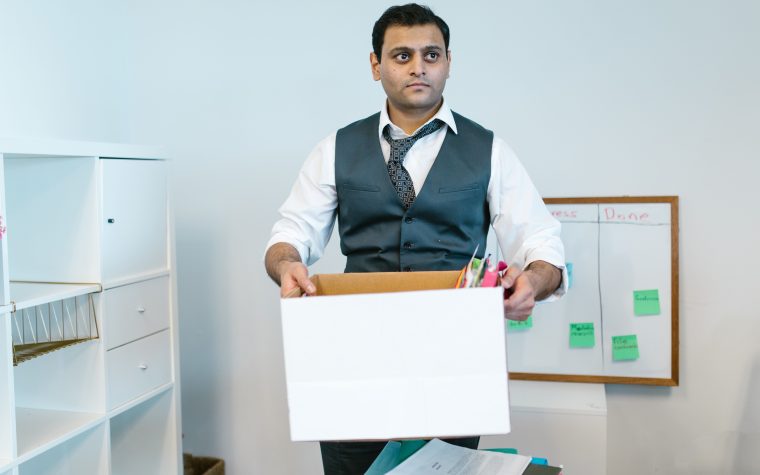 Professional man organizing office belongings in a cardboard box, preparing for transition. Homme professionnel organisant ses affaires de bureau dans une boîte en carton, se préparant à la transition.