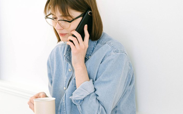 Casually dressed woman talking on phone while holding a coffee mug indoors. Une femme habillée décontractée parlant au téléphone tout en tenant une tasse de café à l'intérieur.