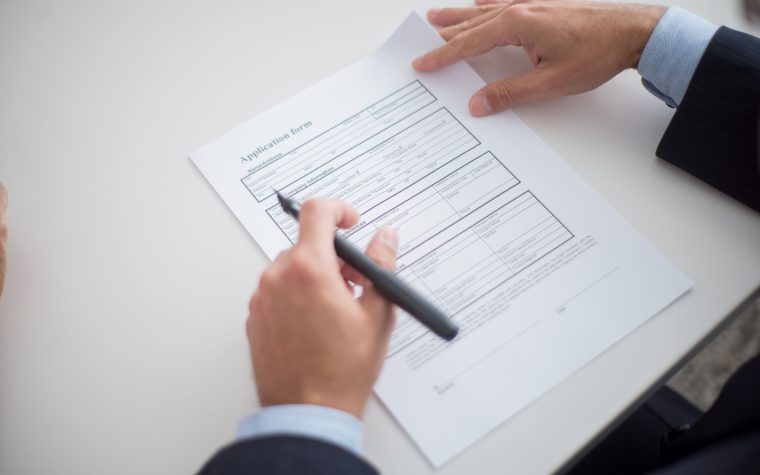 Close-up of a business professional reviewing an application form at a desk. Gros plan d'un professionnel des affaires examinant un formulaire de demande à son bureau.